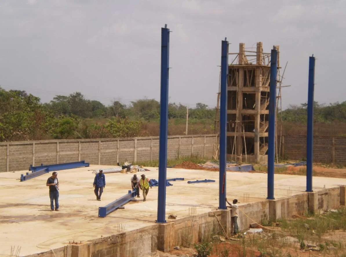 Les ouvriers interviennent au pied des poteaux d’une structure métallique en cours de montage.